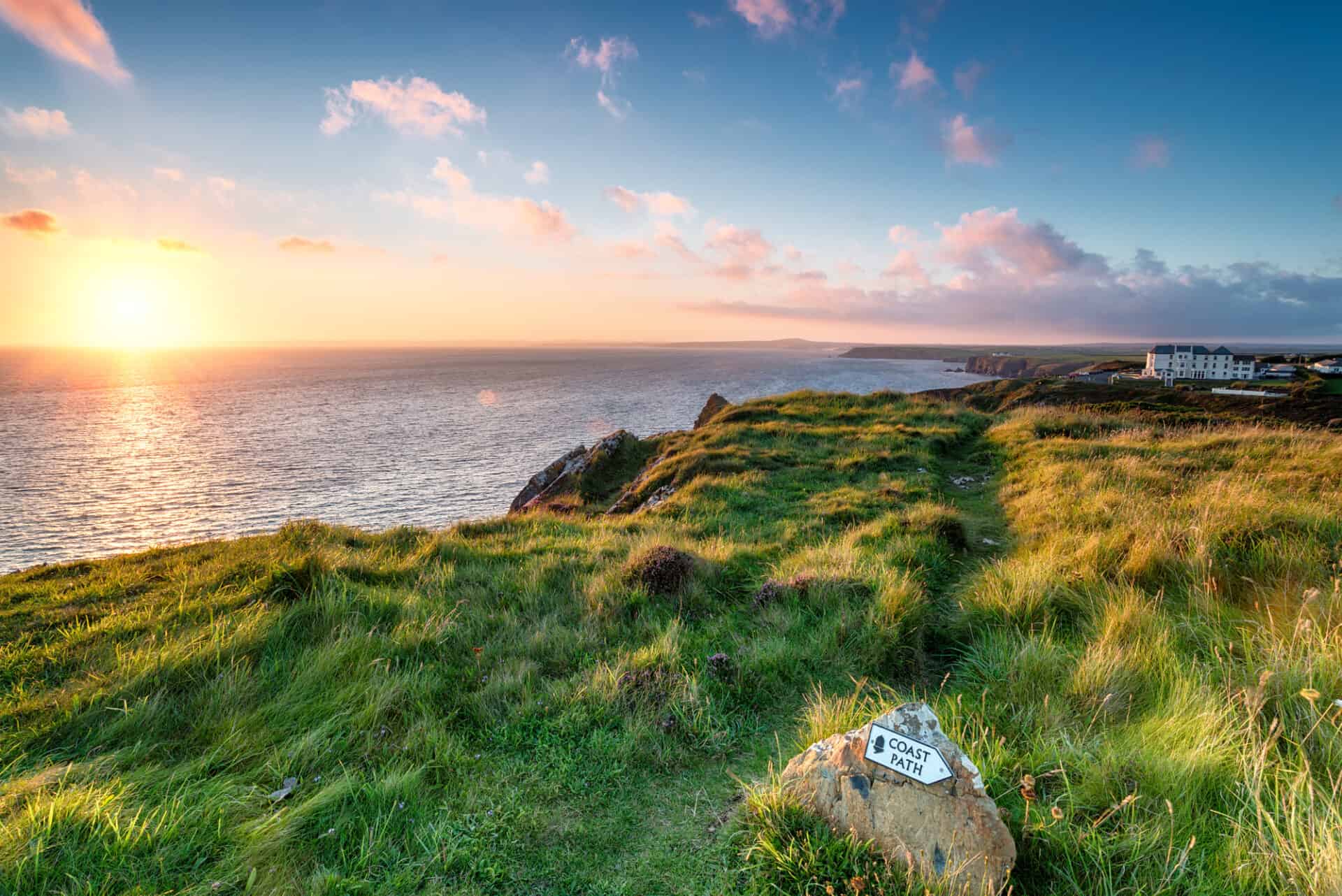 The South West Coast Path on cliffs of cornwall, sea and sunset at horizon