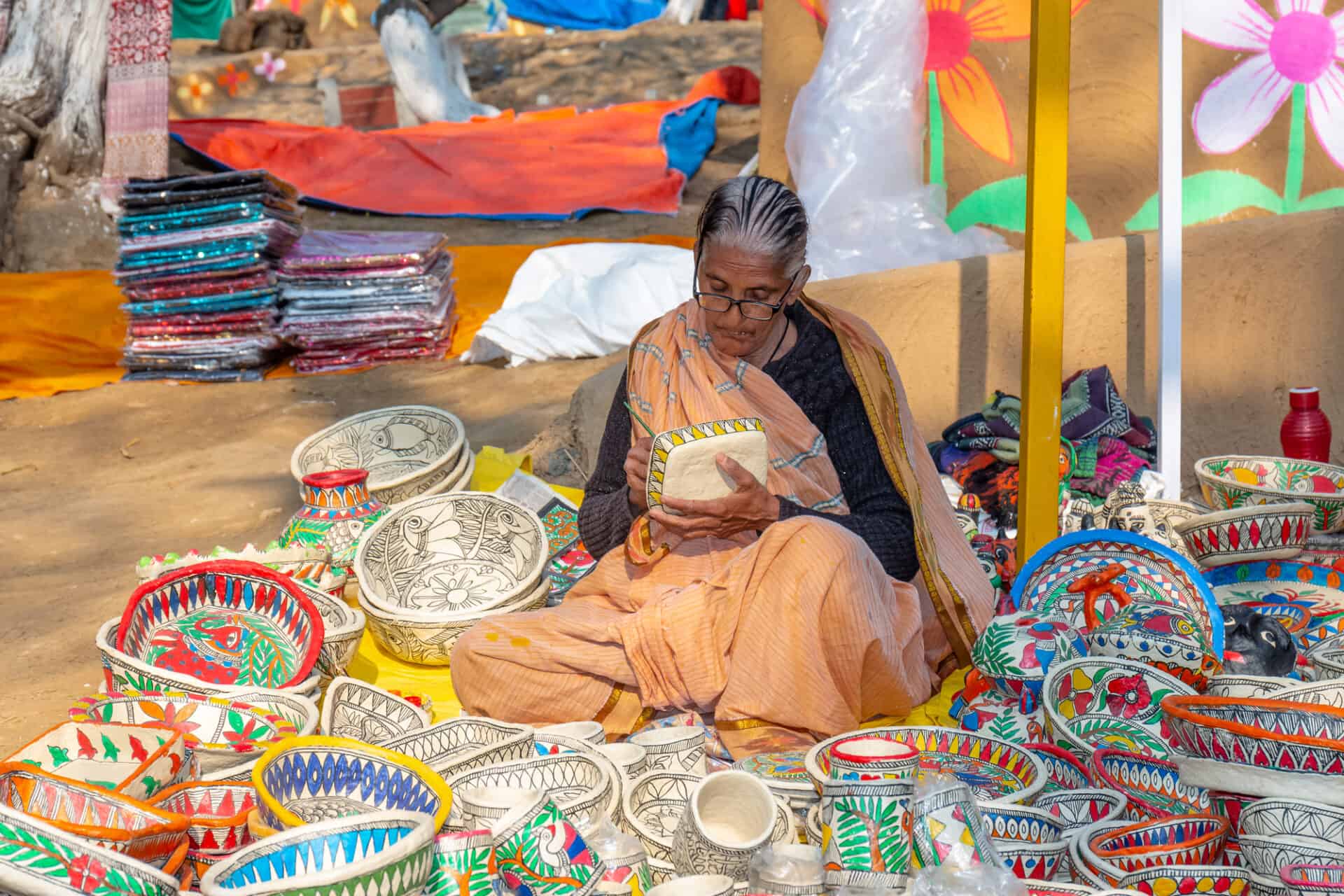 Older Indian woman painting on craft baskets and masks in her shop.