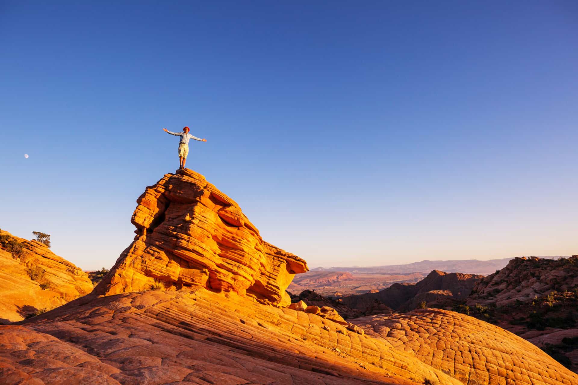 Hiker in Utah mountains, USA, sunlight coloring the mountains orange.