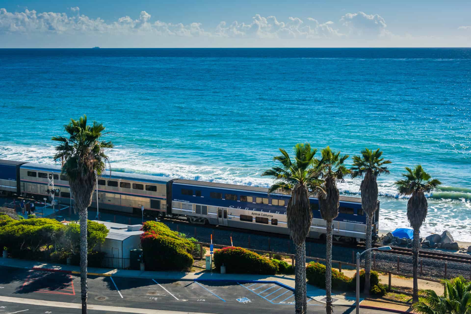 View of a train on a railroad track along the beach with palm trees and Pacific Ocean, California, USA.