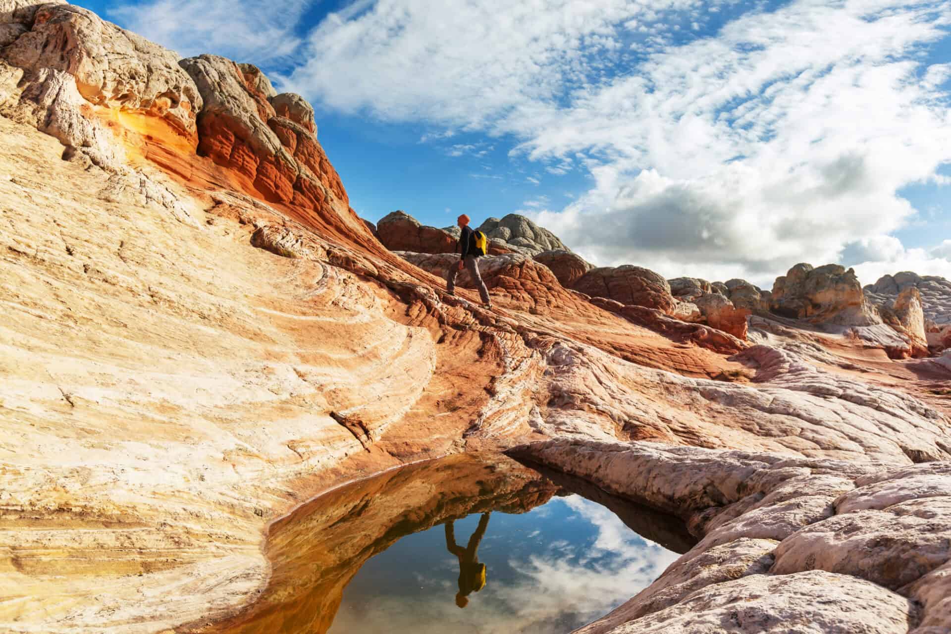 A hiker in the mountains, blue sky and clouds reflected in the water of a small lake